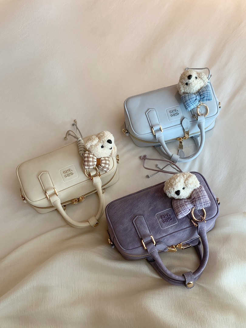 Three small structured handbags in cream, blue, and lavender with teddy bear charms