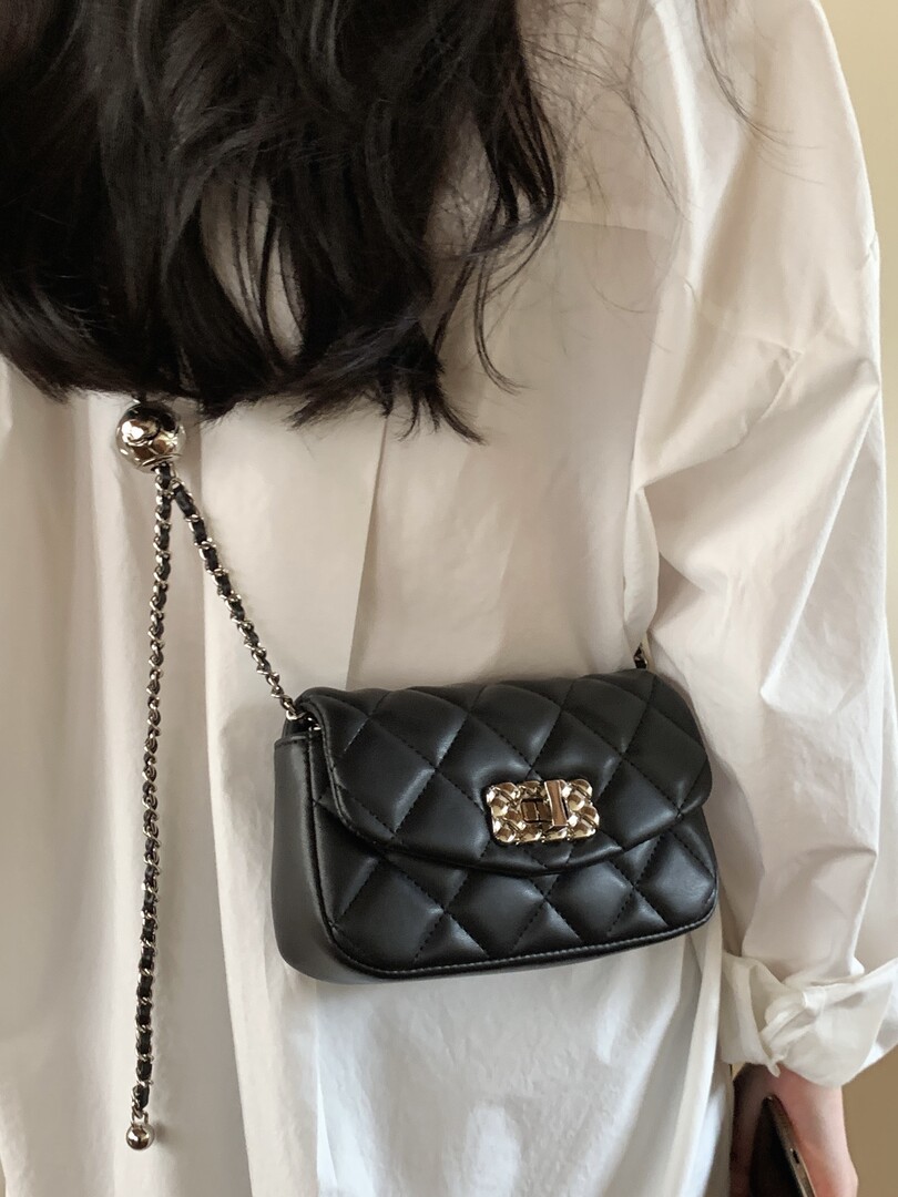 Black quilted chain-strap crossbody bag worn over a white shirt