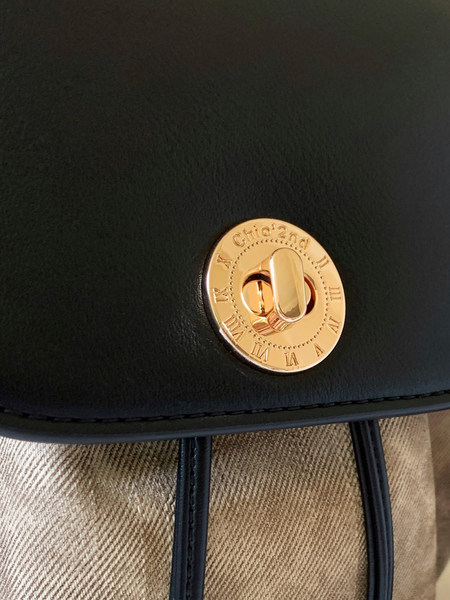 Close-up of a black leather bag with a gold circular clasp