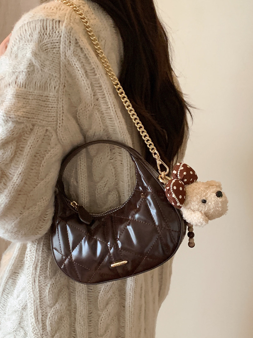 Brown quilted shoulder handbag worn with a cream knit sweater, featuring a teddy bear charm