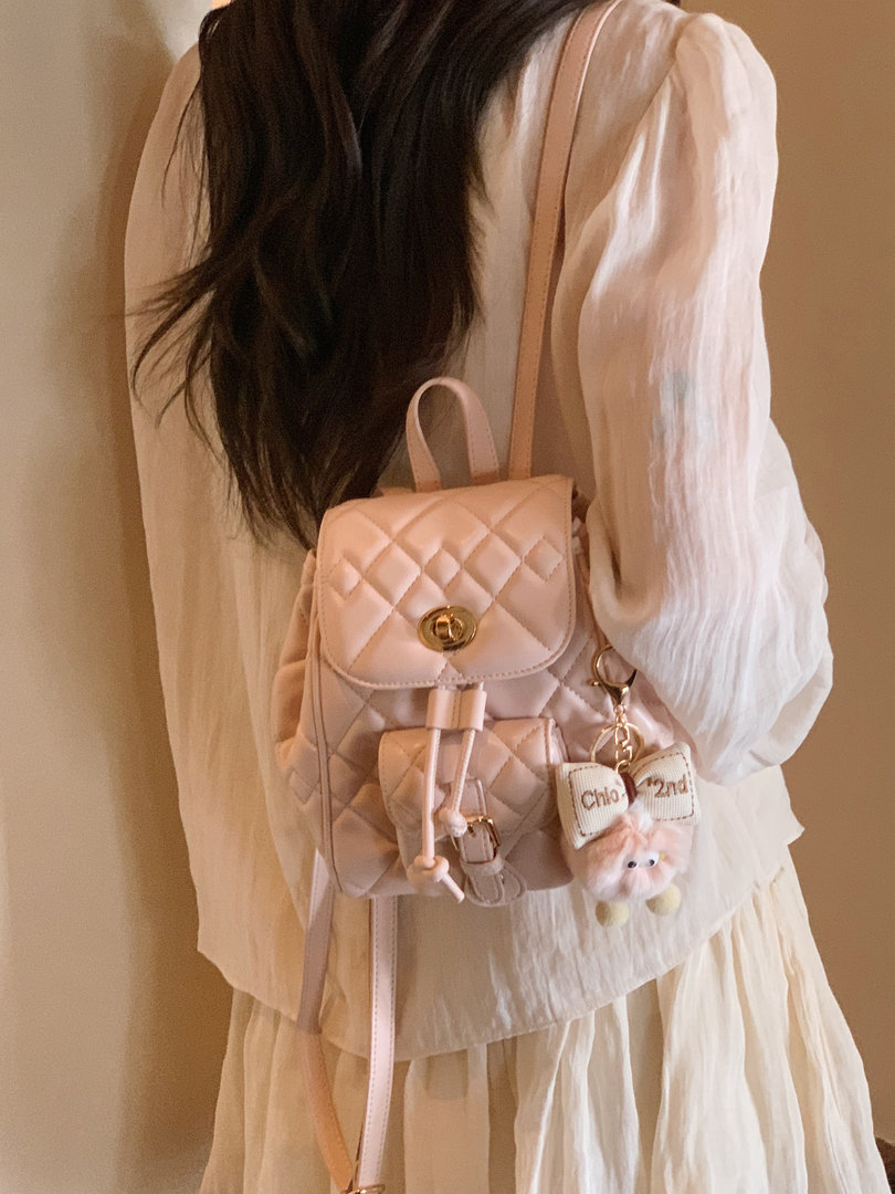 Pink quilted backpack worn on a model with a bow charm