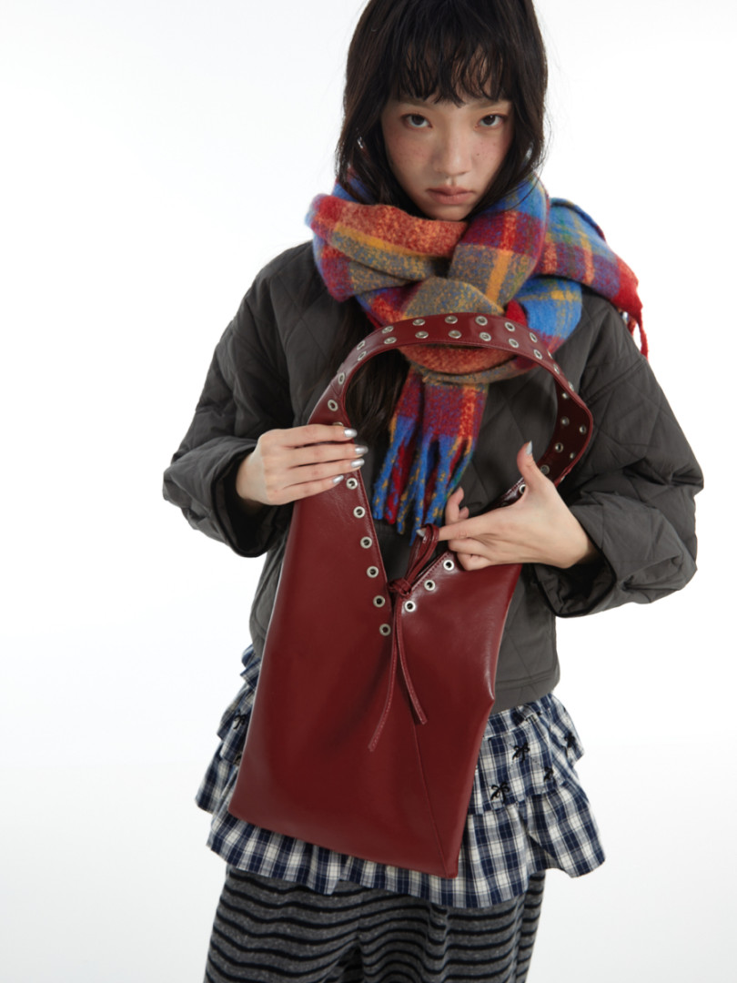 Model holding a red leather tote bag with metal grommets