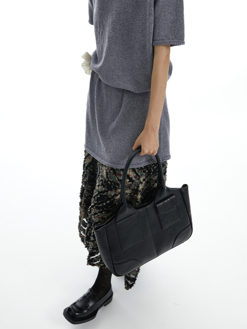 Model wearing a gray outfit and holding a black leather tote bag