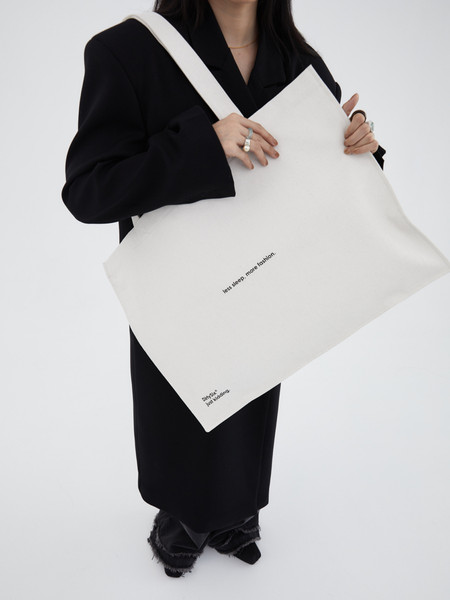 White canvas tote bag with printed text, worn by a model in a black outfit