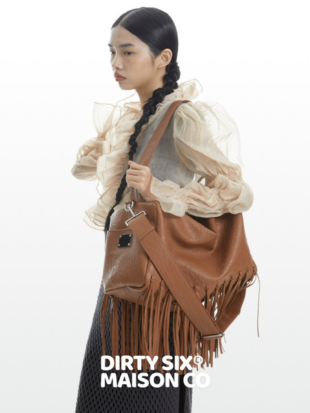 Model wearing a cream ruffled blouse and carrying a large brown fringed leather bag