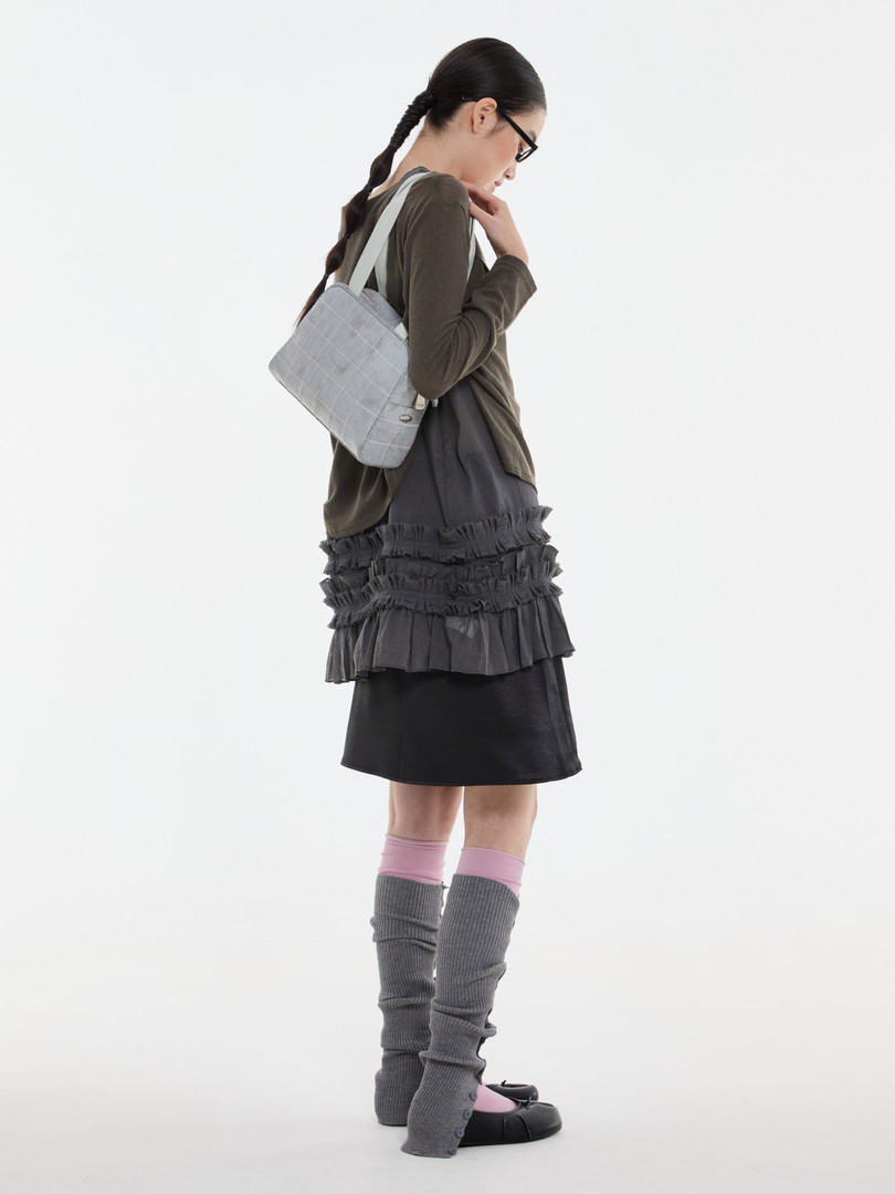 Model wearing a layered dark outfit with a light gray shoulder bag