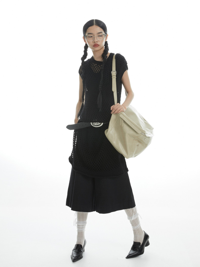 Model wearing a black mesh dress with a beige shoulder bag on a white background