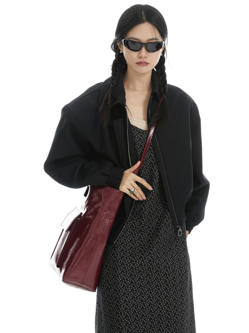Model wearing a black jacket with a patterned dress, sunglasses, and a burgundy tote bag
