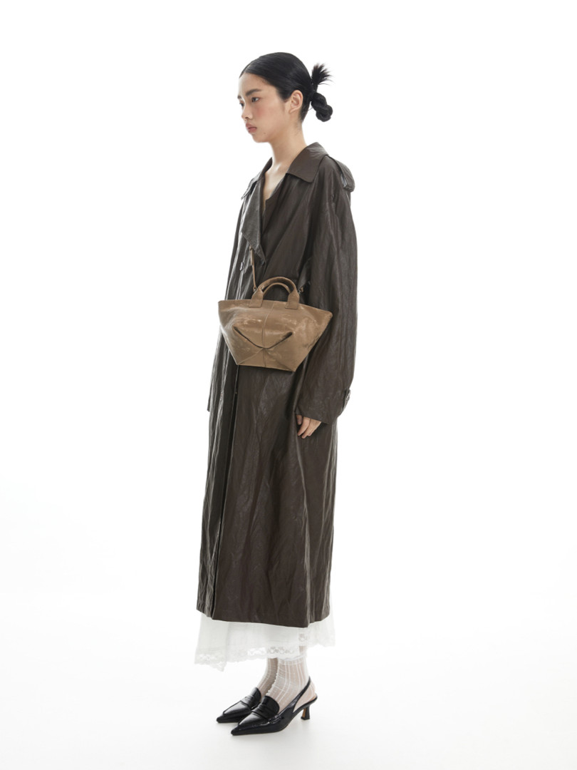 Woman wearing a long dark brown trench coat with a tan handbag