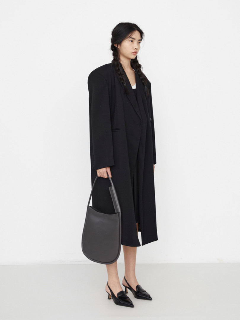 Model wearing a long black coat with a black handbag and pointed heels