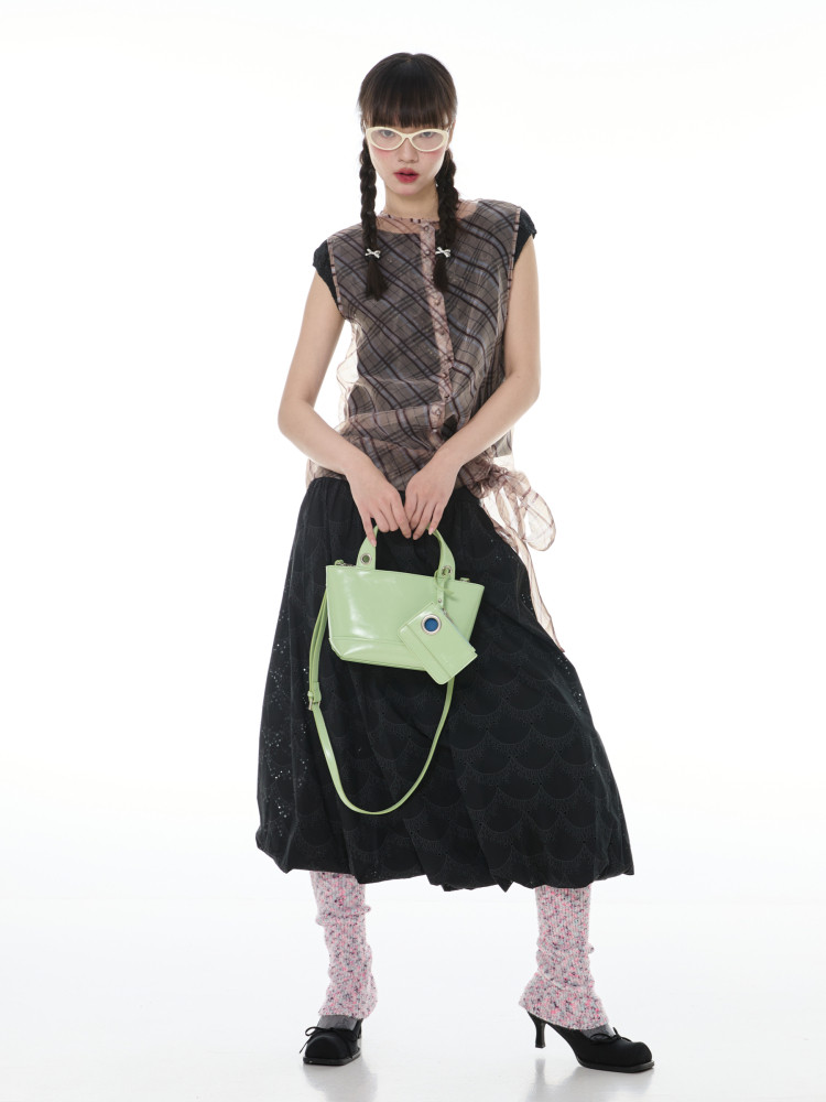 Fashion model wearing a plaid top, black skirt, and holding a light green handbag