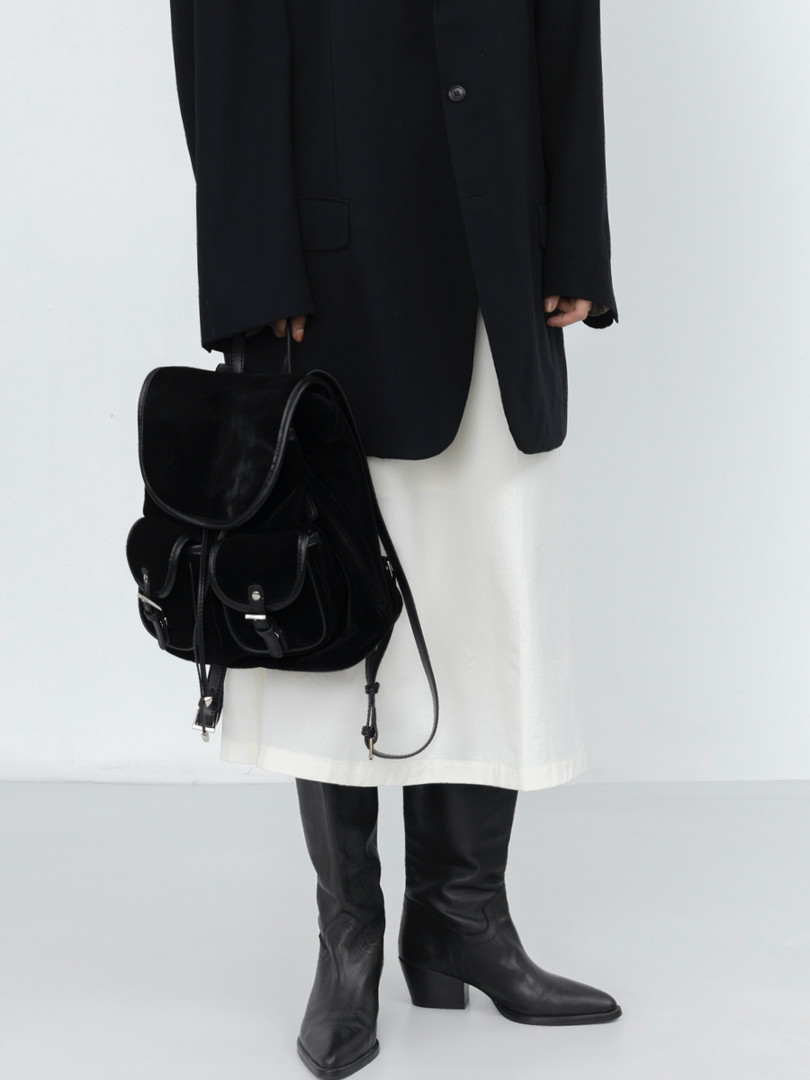 Model wearing a black coat, white skirt, black knee-high boots, and a black backpack