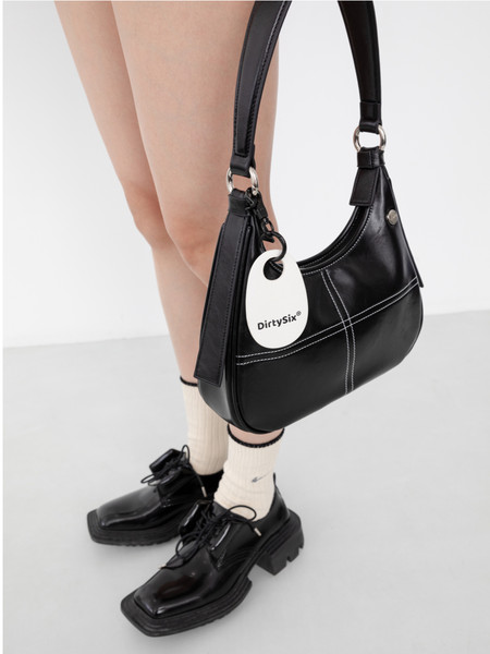Black leather shoulder handbag worn with black loafers on a model