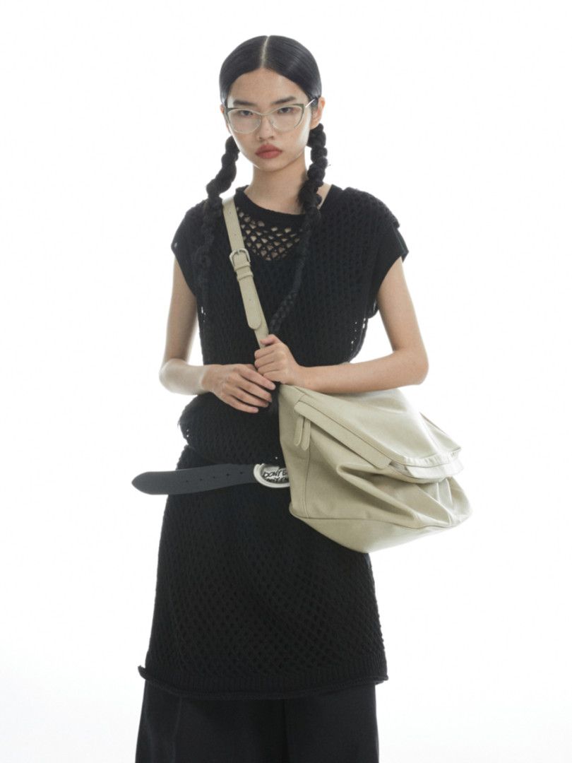 Model wearing a black sleeveless dress with a light beige shoulder bag
