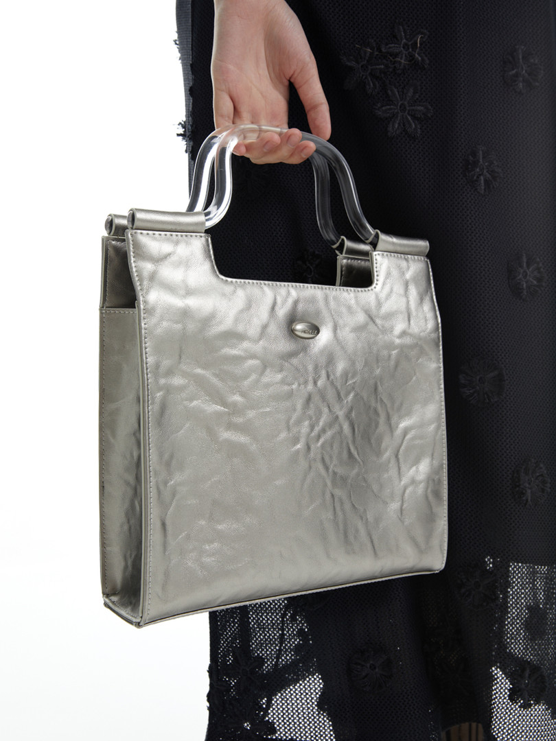 Silver metallic handbag with clear handles being held by a person