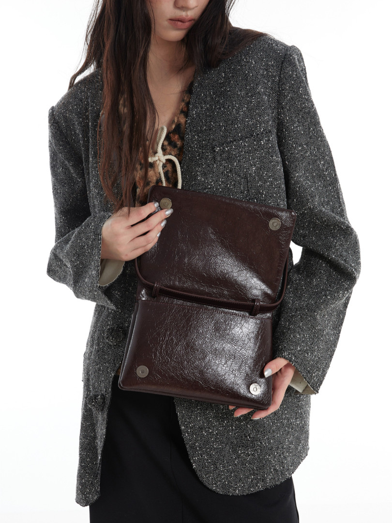 Model holding a dark brown leather shoulder bag on a white background