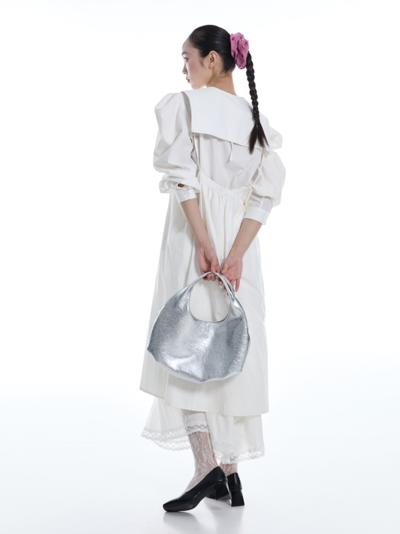 Model wearing a white long-sleeve dress and holding a silver handbag