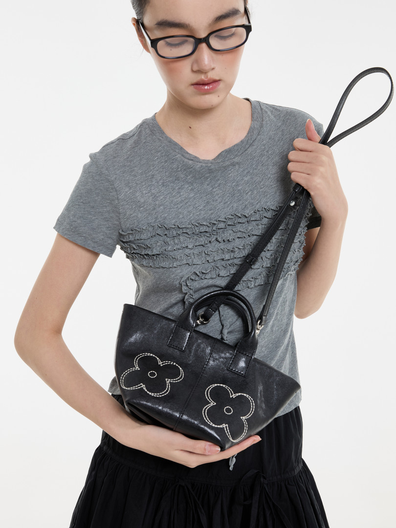 Model wearing a gray ruffled T-shirt and holding a black floral handbag