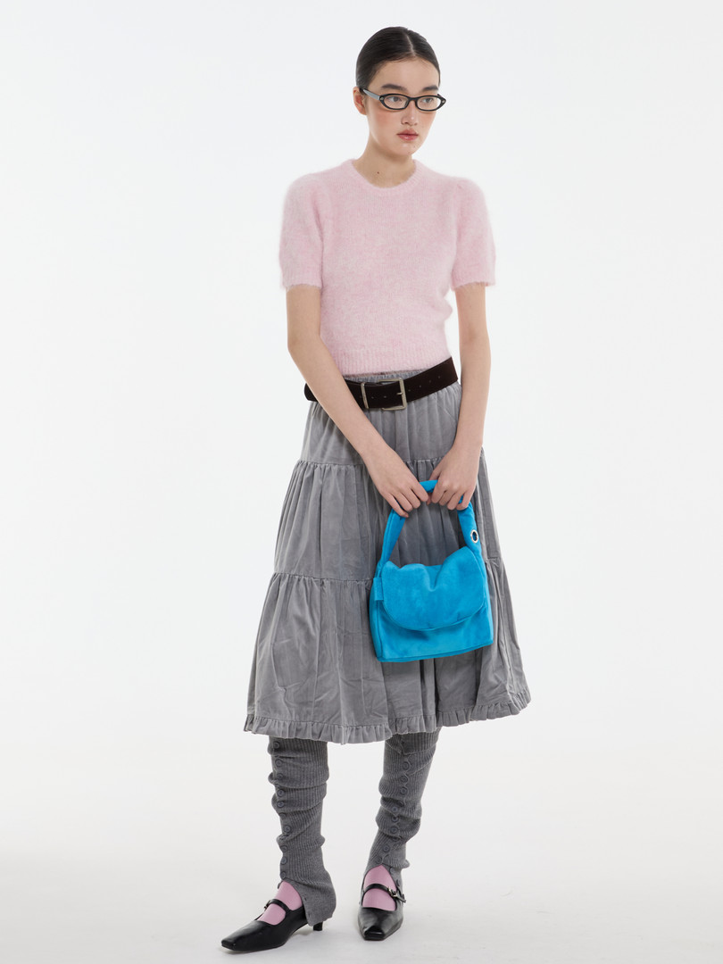 Model wearing a pink short-sleeve knit top, gray tiered skirt, and carrying a bright blue handbag