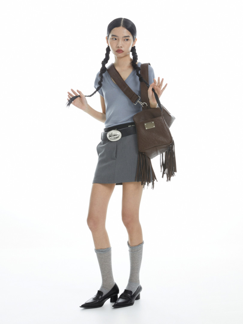 Model wearing a blue top, gray mini skirt, brown crossbody bag, and loafers