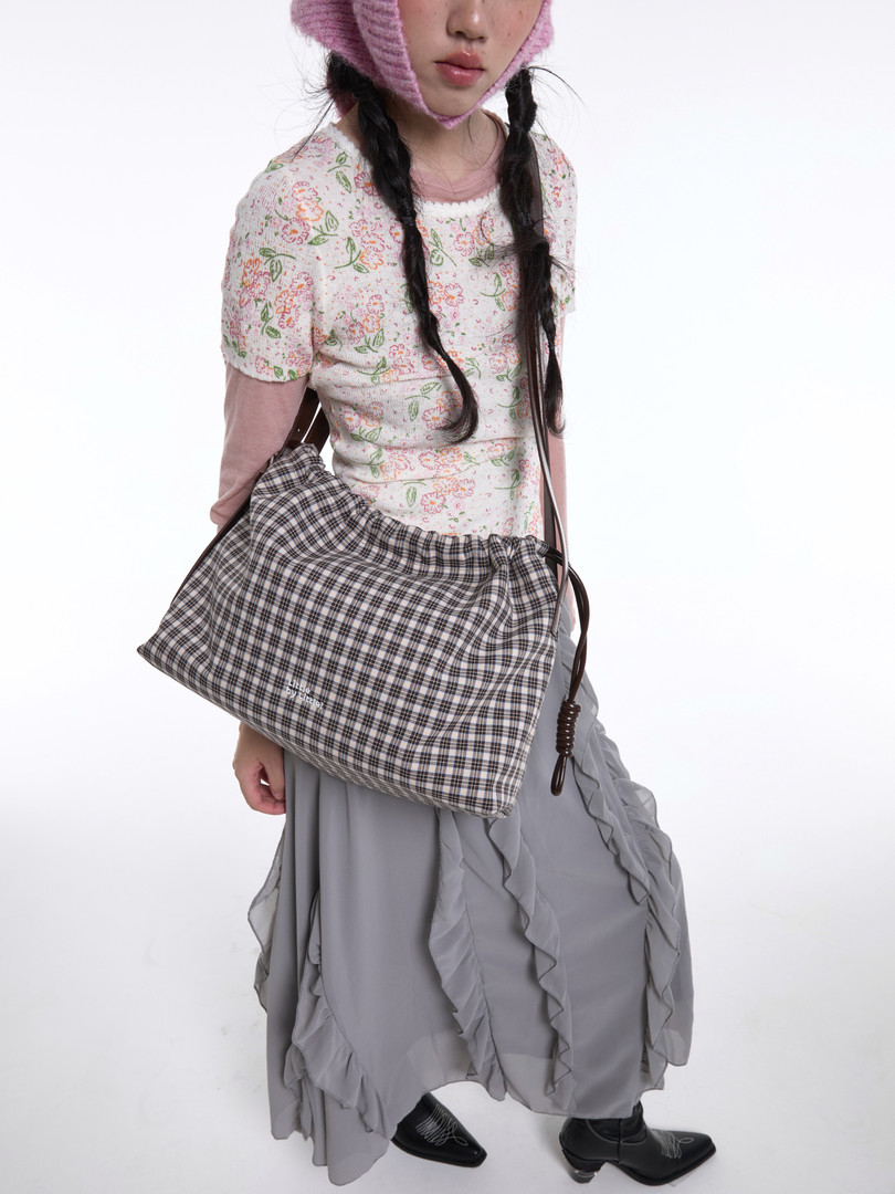 Model wearing a plaid shoulder bag with a floral top and gray skirt