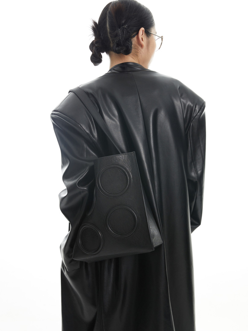 Black faux leather coat worn by a model with a matching black shoulder bag