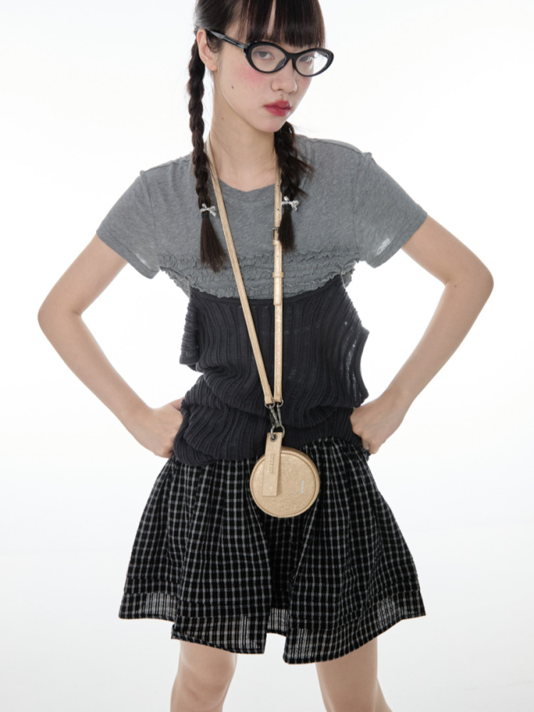 Model wearing a layered gray and black casual outfit with a plaid skirt and crossbody accessory