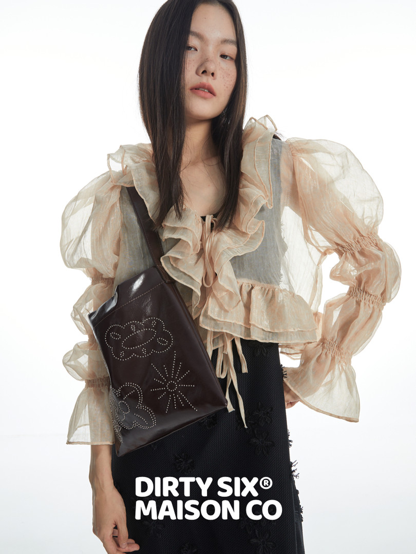 Model wearing a sheer ruffled blouse and black skirt with a dark crossbody bag