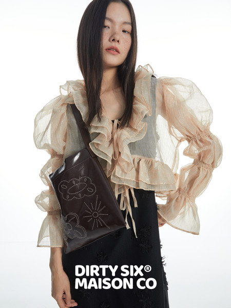 Model wearing a sheer ruffled blouse and black skirt with a dark crossbody bag