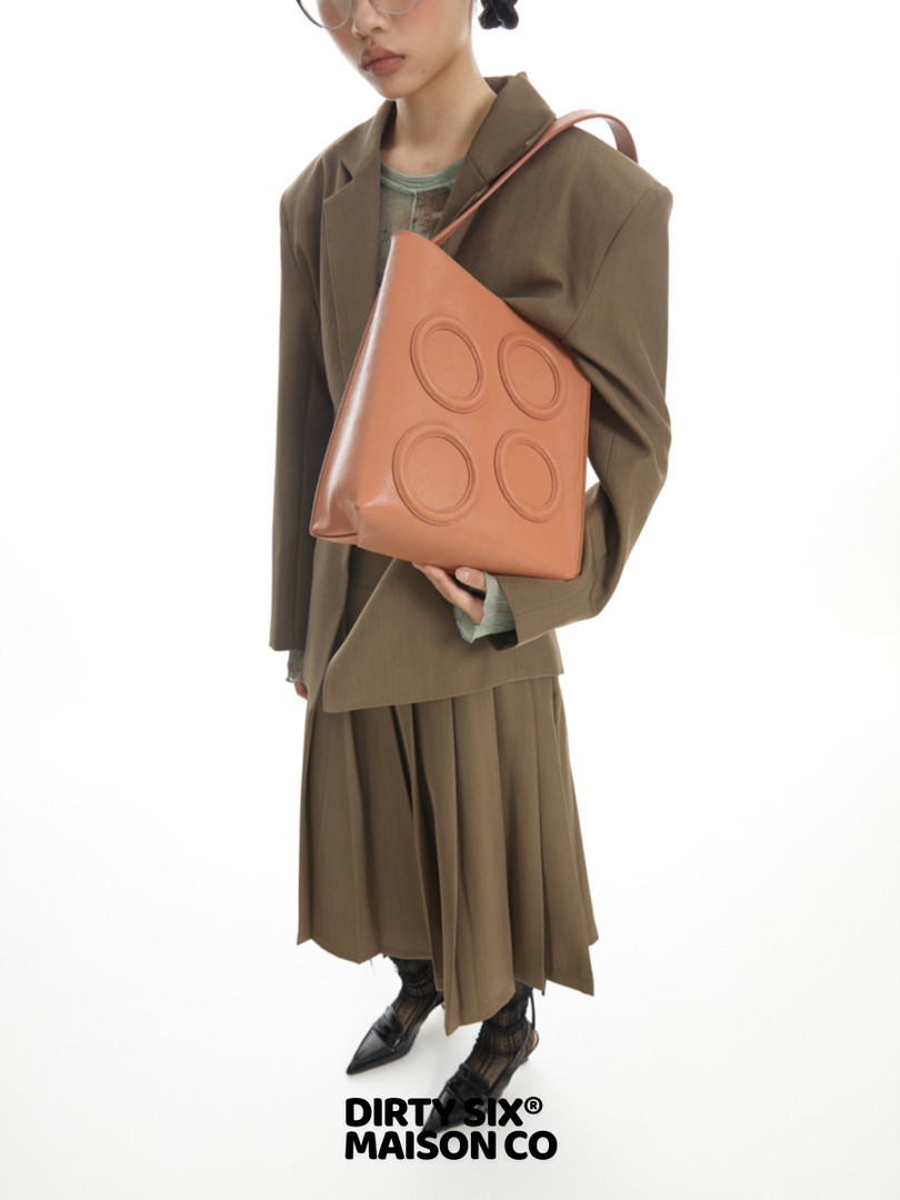 Model wearing an olive-brown outfit and holding a tan leather tote bag