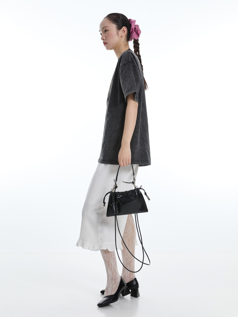 Model wearing a black oversized top, white skirt, lace tights, black heels, and carrying a black handbag