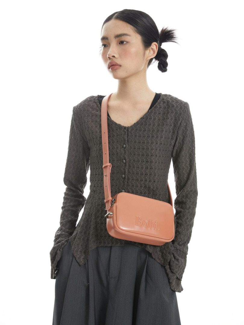 Model wearing a dark textured long-sleeve top with a peach crossbody bag.