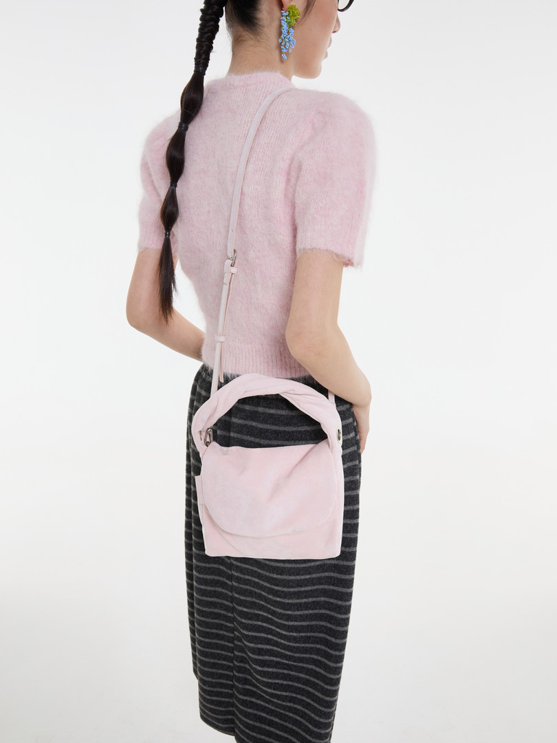 Model wearing a pink fuzzy short-sleeve top with a small pink crossbody bag and striped skirt