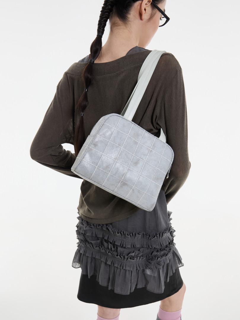 Model wearing a light gray quilted shoulder bag over a dark outfit