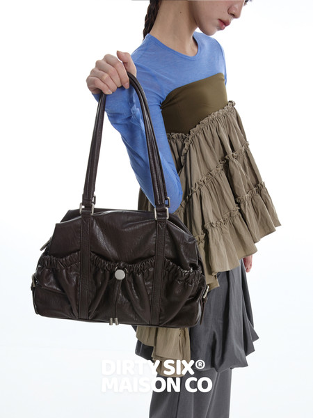 Model holding a black leather handbag while wearing a layered fashion outfit