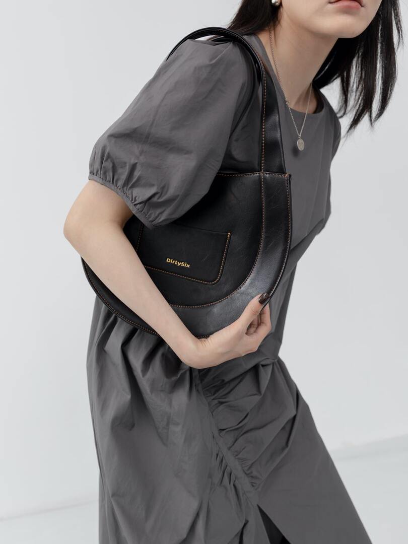 Black leather shoulder bag worn by a model with a gray dress