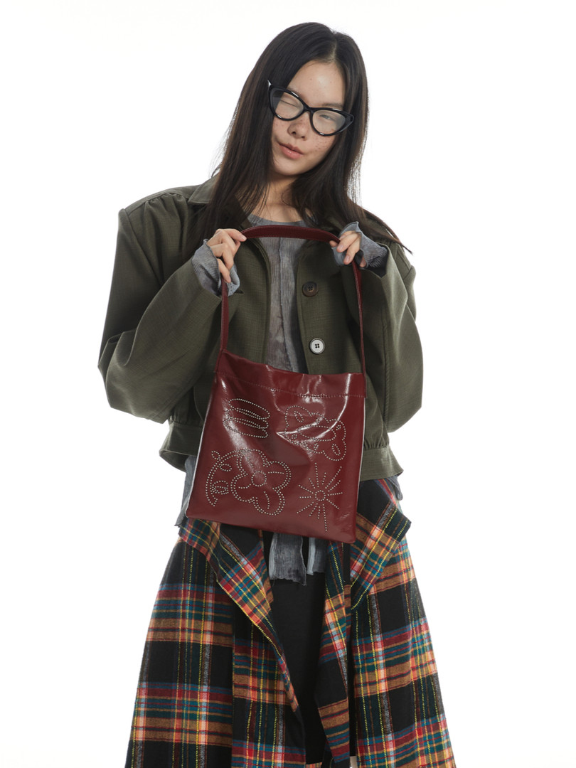 Model holding a burgundy leather shoulder bag with floral detailing