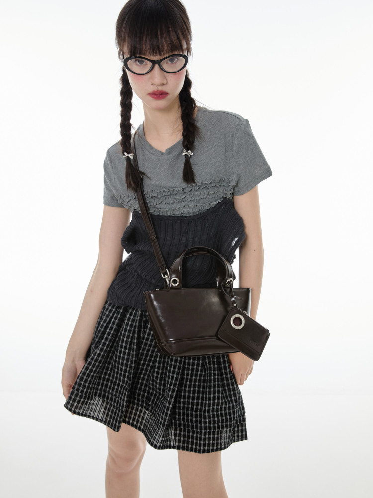 Model wearing a grey top, black skirt, and brown handbag