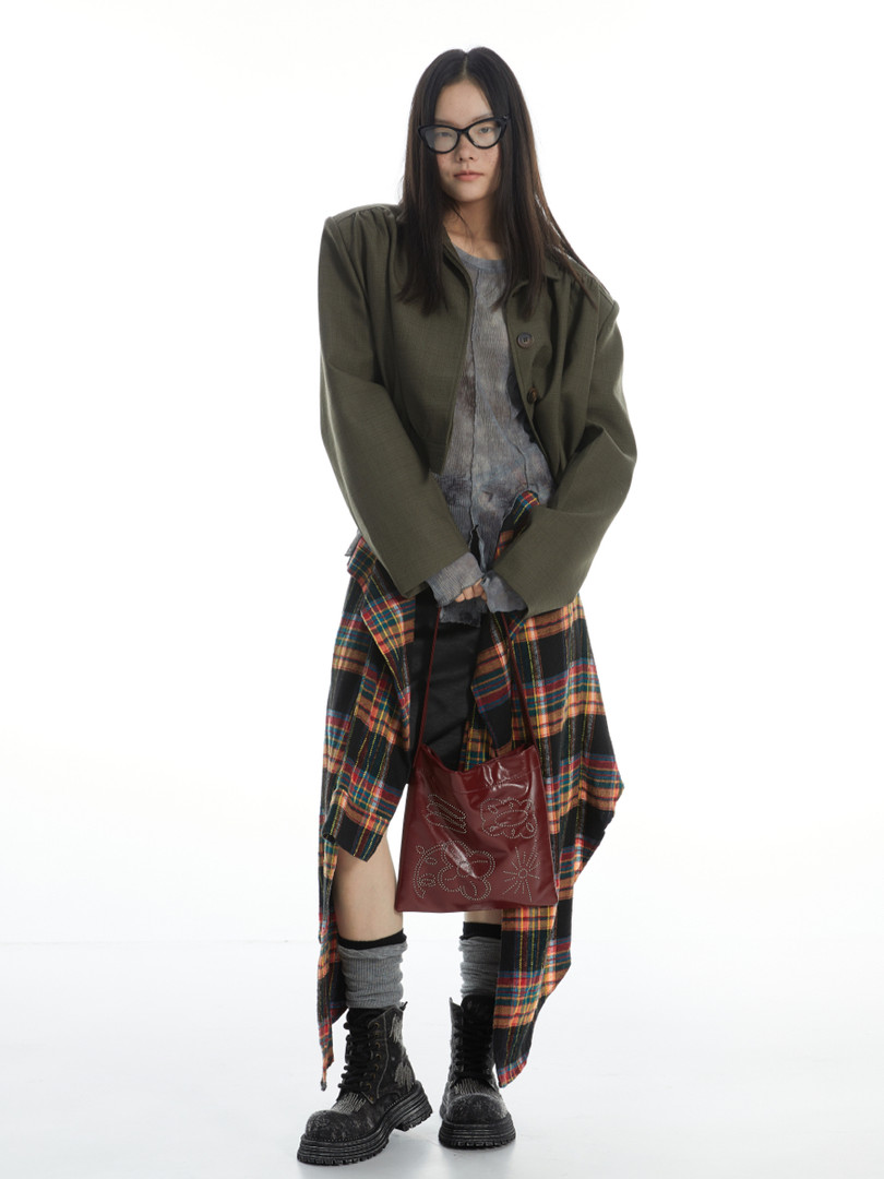 Fashion model wearing layered streetwear outfit with olive jacket, plaid shirt, and boots