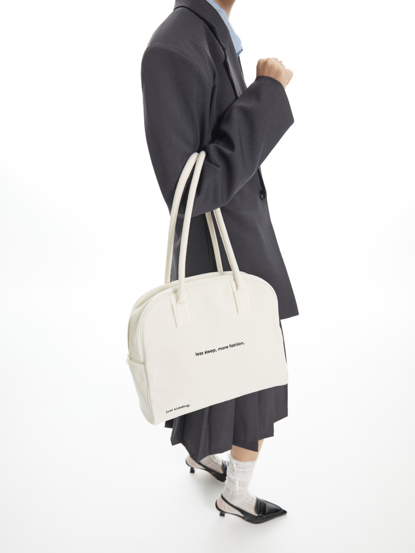 White tote bag with text, worn by a model in a dark outfit