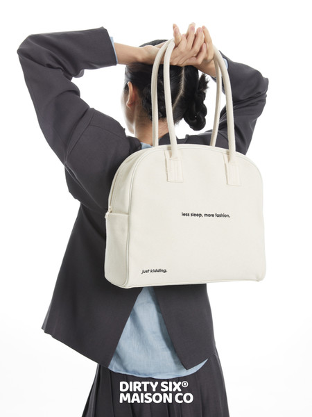 Cream tote handbag worn by a model with printed text detail
