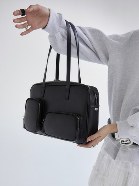 Black rectangular leather handbag with long straps and front pockets held by a person
