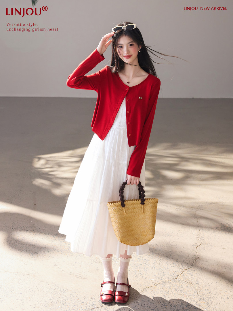 Woman modeling a red cardigan over a white dress with a straw handbag