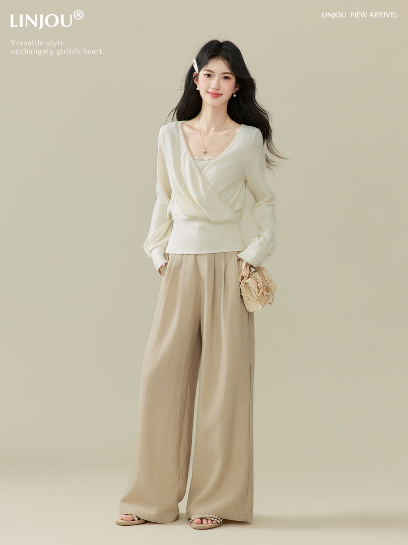 Model wearing a cream wrap top with wide-leg beige trousers and a small handbag
