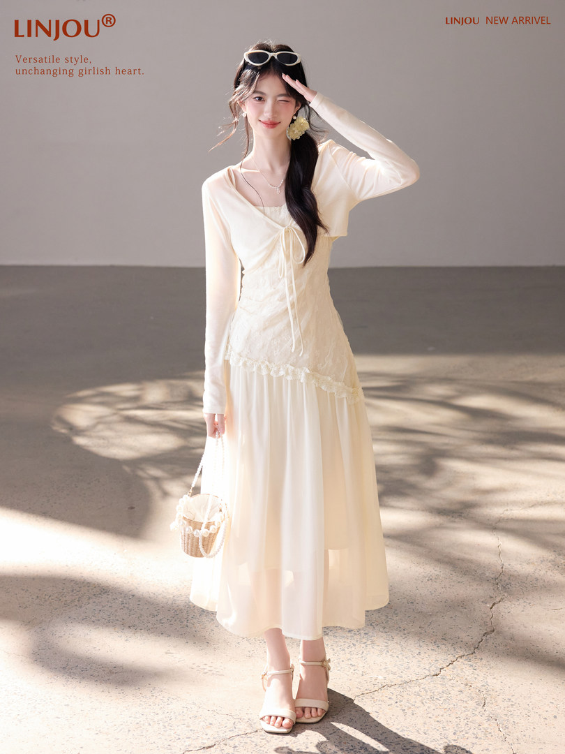 Model wearing a cream long-sleeve maxi dress with lace details and a small woven bag
