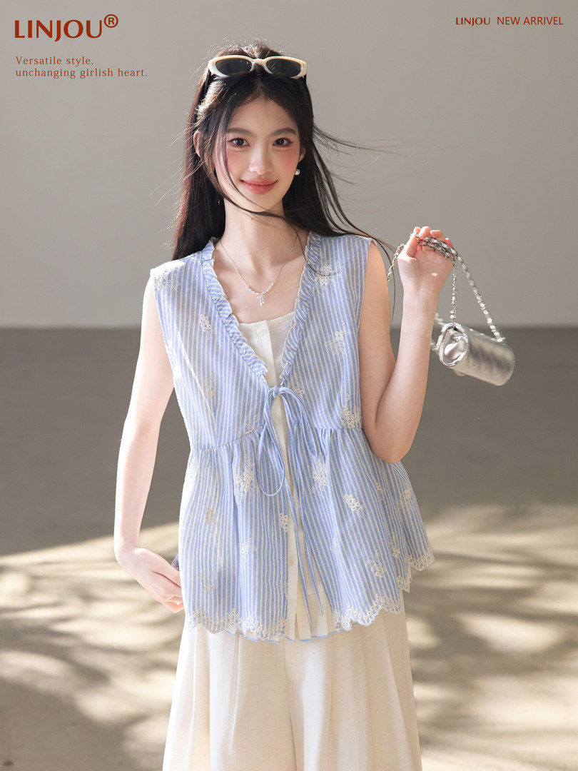 Model wearing a light blue striped sleeveless vest over a cream dress, holding a small silver bag