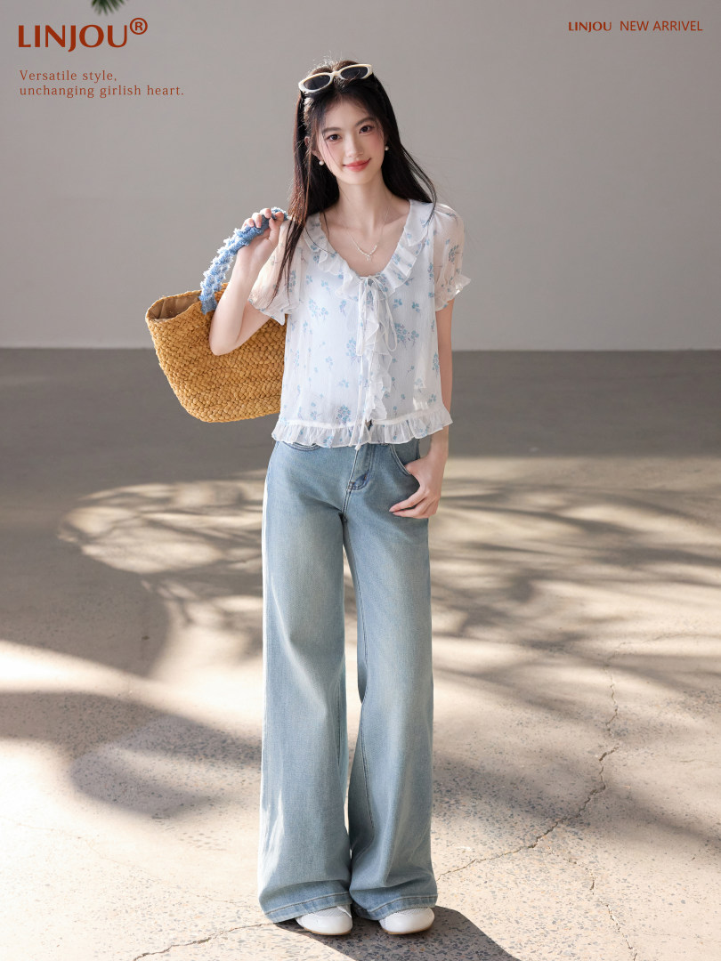 Model wearing a white floral ruffled blouse with light blue wide-leg jeans and a woven straw bag