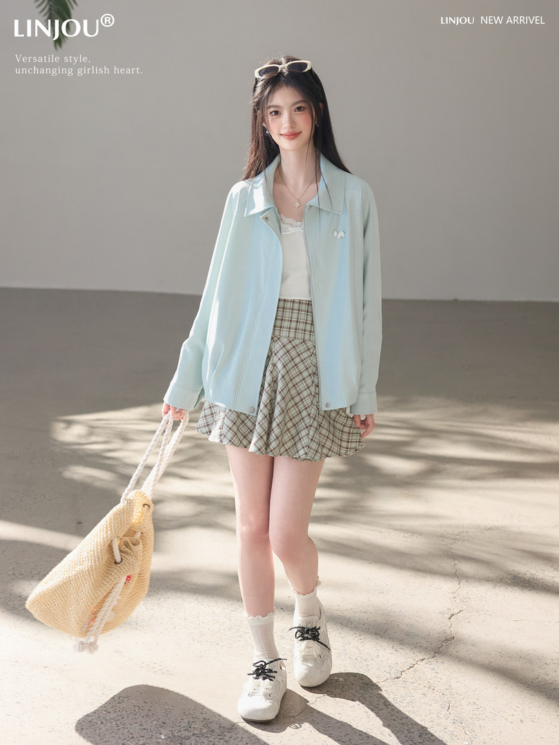 Model wearing a light blue jacket with a plaid skirt and woven tote bag