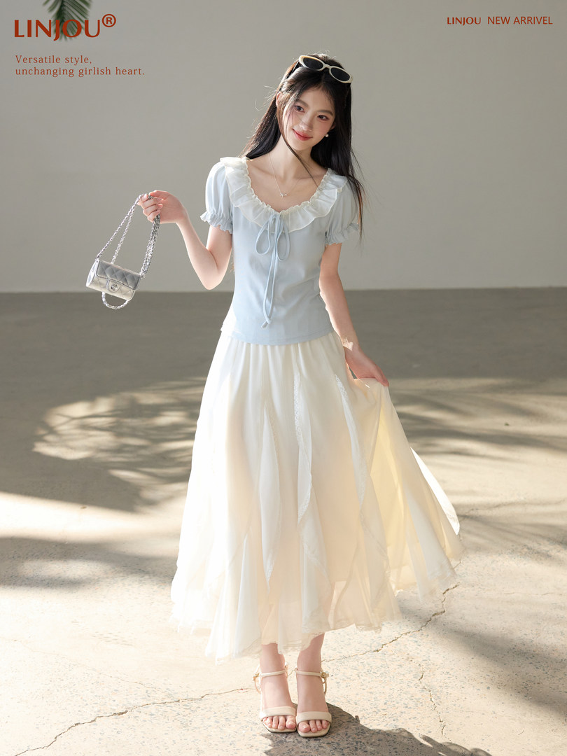 Woman wearing a light blue ruffled top with a flowing white skirt and small shoulder bag