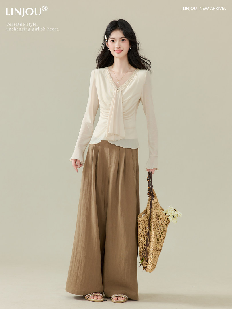 Model wearing a cream lace-trim blouse with wide-leg brown pants and a woven bag